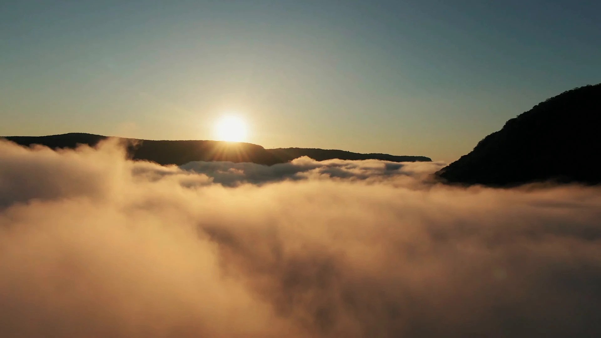 Golden sunlight above a mountain ridge and a sea of soft mist.